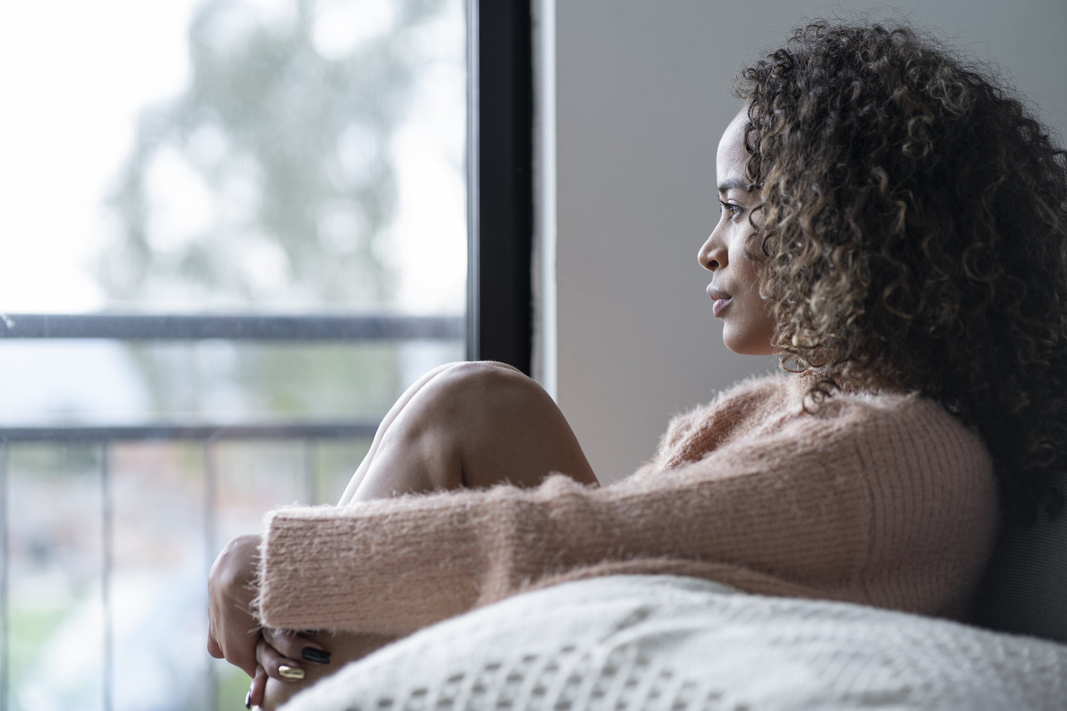 Black woman in her 20s sitting in the living room of her house looking away, very somber by her ADHD, PTSD and loneliness.