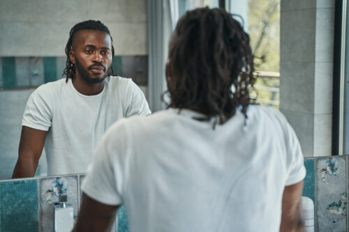 Portrait of serious focused man looking down at his reflection in wall-mounted mirror