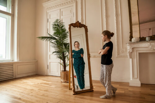 Teen girl looking at mirror and sees middle age woman in reflection symbolizing the way our trauma can stay with us