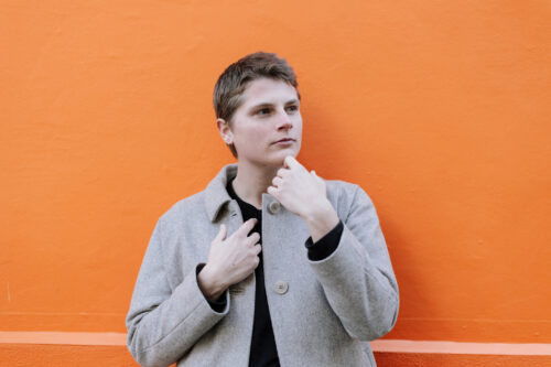 Individual leaning against an orange wall, lost in thought