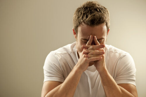 A young man leaning on his head in his hands distraught with grief, reliving, negative thoughts, and feeling on edge