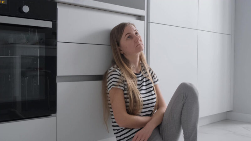 Unhappy girl sitting on kitchen floor feeling depressed.