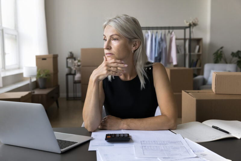 Thoughtful serious businesswoman sit at desk with laptop, feeling overwhelmed by her in ability to focus