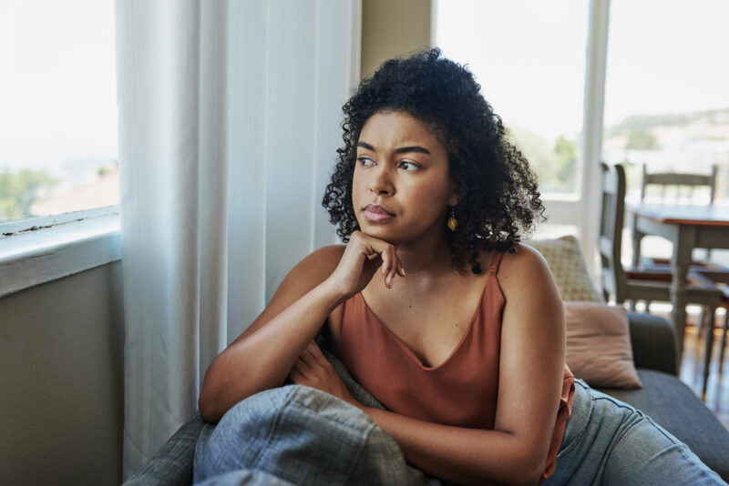 Shot of a young woman looking pensively out a window at home considering whether or not she's exhibiting signs of narcissism