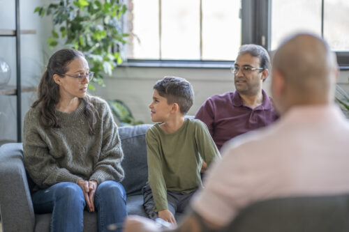 A family of three sit on a couch in front of a councillor and discuss behavioral health struggles in an urban office space.