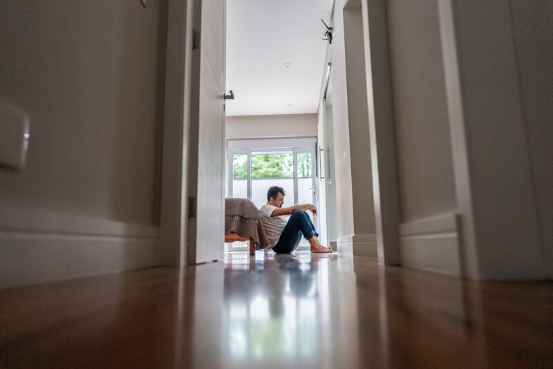 Sad mature man feeling bad sitting on the floor in the bedroom at home