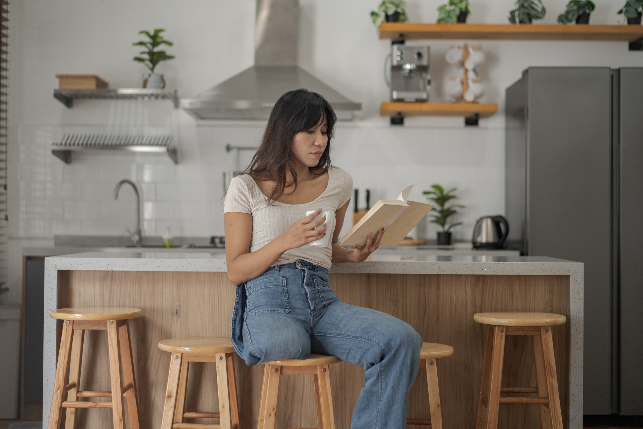 Woman sits in kitchen enjoying a cup of coffee and reading her book.